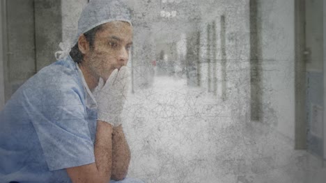 Textured-scratched-overlay-against-stressed-caucasian-male-health-worker-sitting-at-hospital