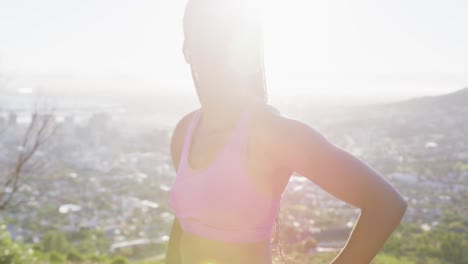 African-american-woman-exercising-outdoors-wearing-wireless-earphones-using-watch-in-countryside