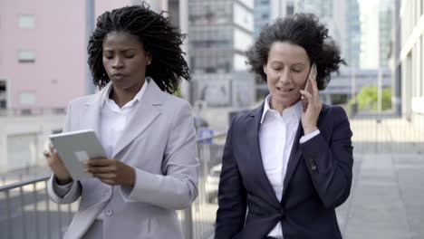 mujeres de negocios serias con teléfonos inteligentes y tabletas