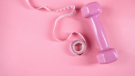 pesas rosas y cinta métrica sobre un fondo rosado