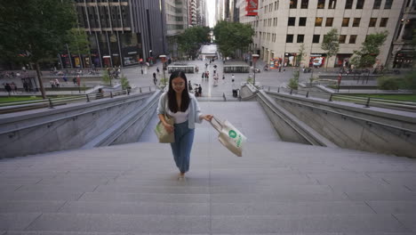young woman walking up wide city stairs with bags in an urban setting