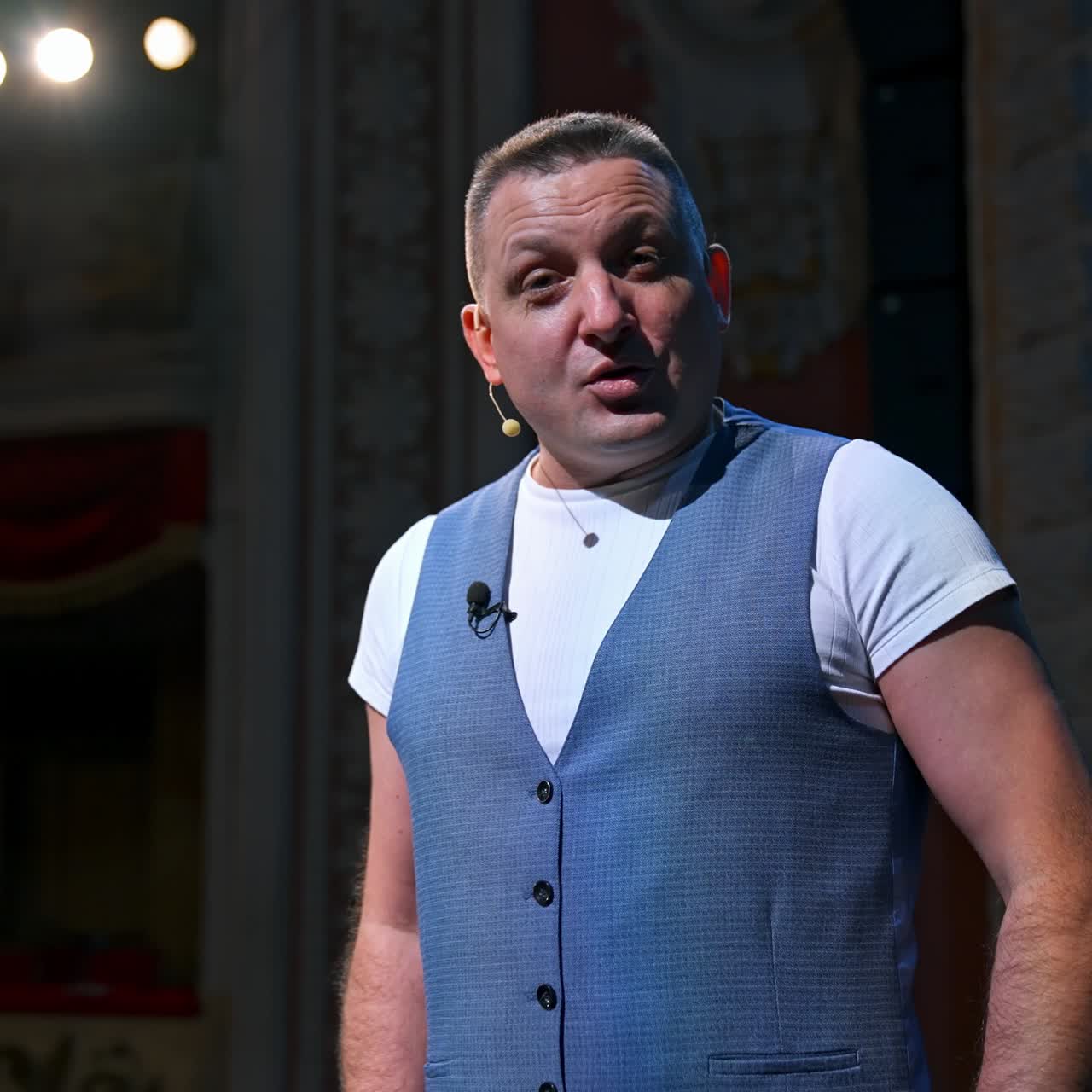 Portrait of an actor during the rehearsal. Man in grey suit standing on stage in the empty theater and talking to camera. Lockdown and world crisis