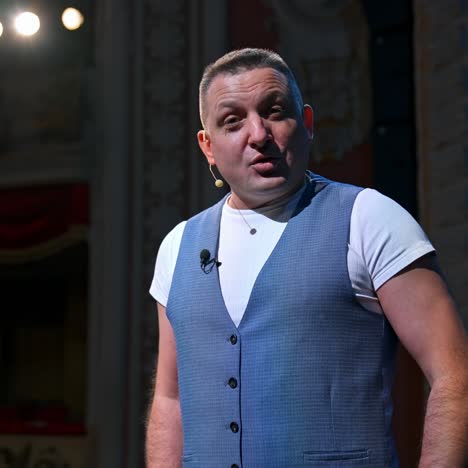 portrait of an actor during the rehearsal. man in grey suit standing on stage in the empty theater and talking to camera. lockdown and world crisis