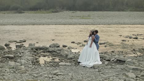 Wedding-couple-standing-near-mountain-river.-Groom-and-bride-in-love