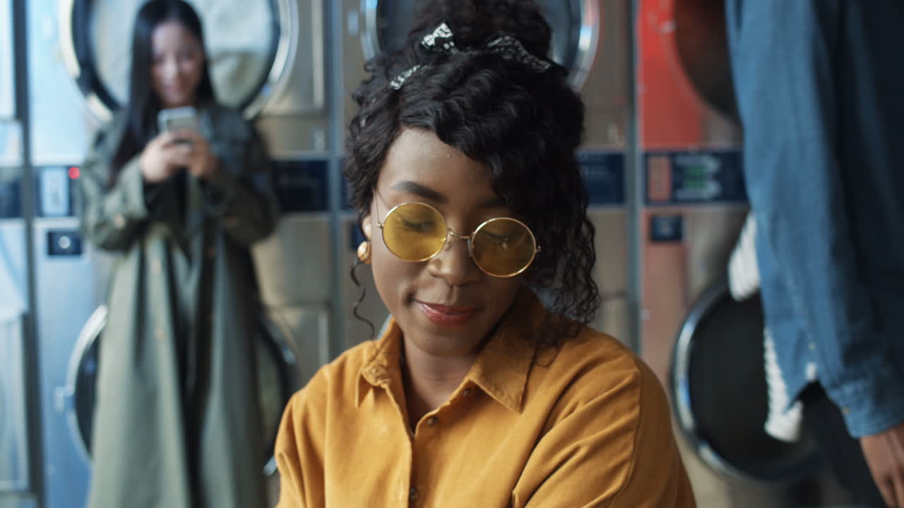 빨대로 오렌지 주스를 마시고, 쉬고, 빨래할 옷을 기다리는 노란색 안경을 쓴 예쁘고 행복한 소녀