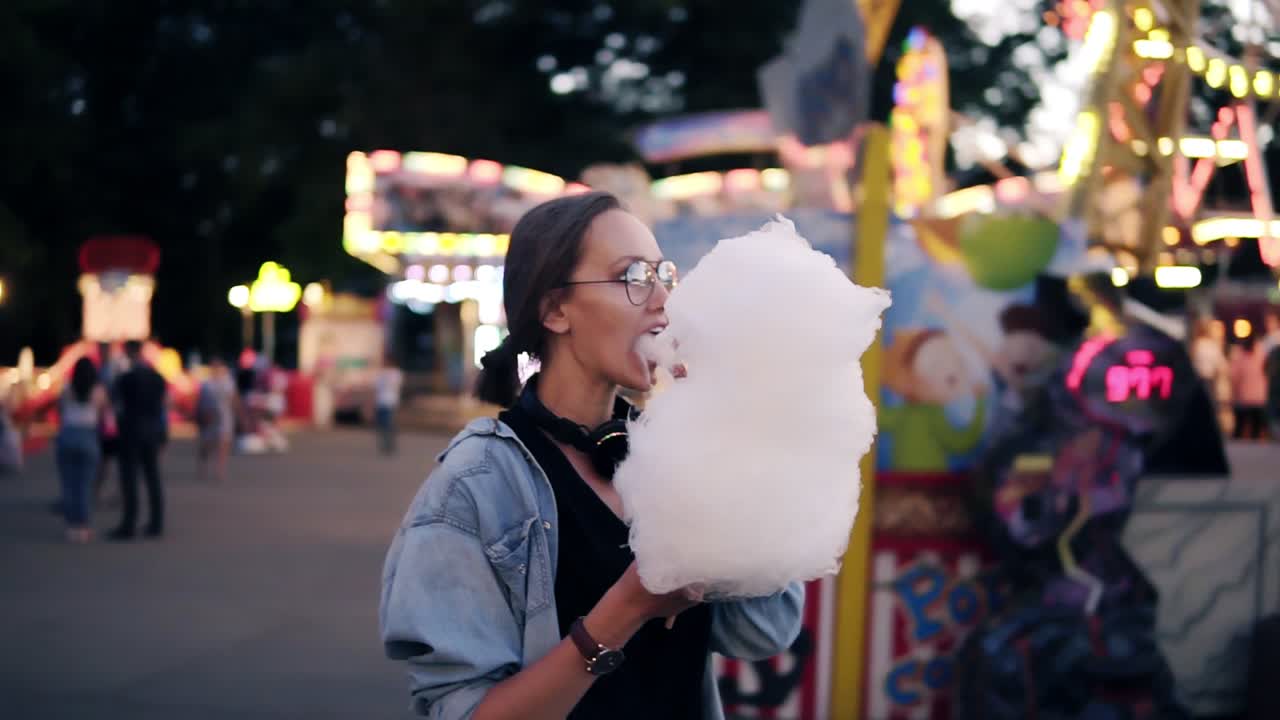 feliz, mujer joven caminando en el parque de atracciones en verano. mujer rubia tomando algodón de azúcar, disfrutar de su tiempo, sonriendo