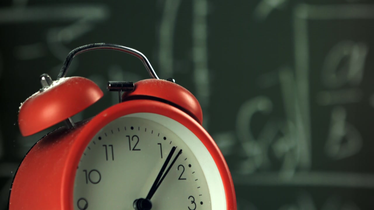 Red Alarm Clock Ticking with Dust Falling in Front of a Chalkboard