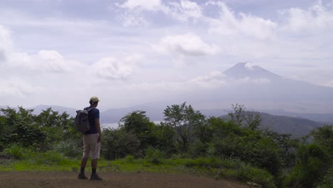 Male-hiker-walking-into-frame-on-top-of-Mountain-looking-out-towards-silhouette-of-Mt