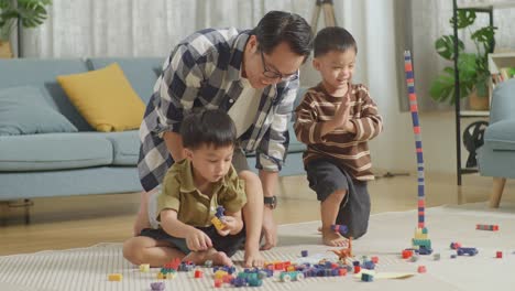 full body of asian father and sons assemble the construction set colorful plastic toy brick on a mat at home