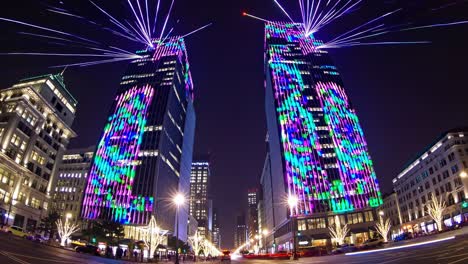 colorful light projections transforming the facades of modern skyscrapers, creating a vibrant and dynamic urban nightscape with light trails from moving cars