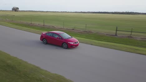 aerial view of red sports car frontal view driving through empty country road at sunset