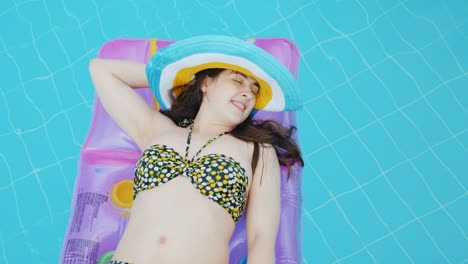 모자를 입은 매력적인 젊은 여성이 수영장에서 부풀이 매트리스에 떠다니고 있습니다. 이상적인 휴가 개념