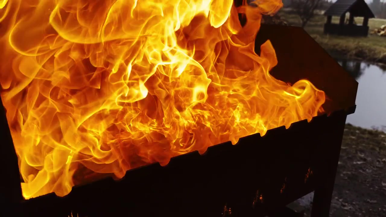 Grandi fiamme che si alzano da un barbecue da esterno con carboni ardenti.