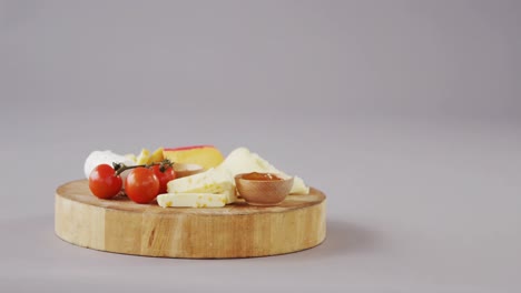 Different-types-of-cheese,-tomatoes-and-bowl-of-jam-on-wooden-board