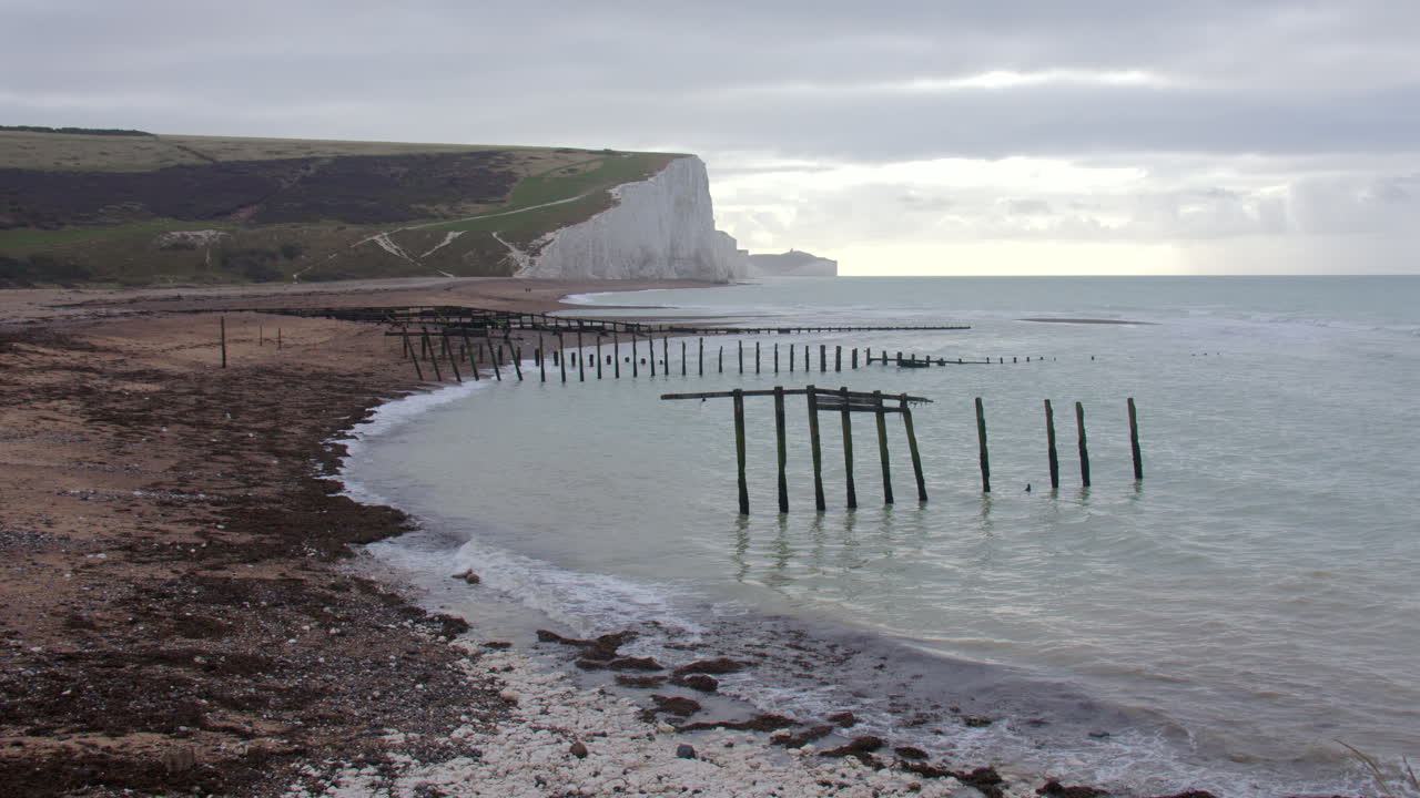 Inquadratura panoramica delle scogliere delle Sette Sorelle dalla spiaggia con pennelli frangiflutti rotti sulla spiaggia di Cuckmere Haven, vicino a Seaford Head.