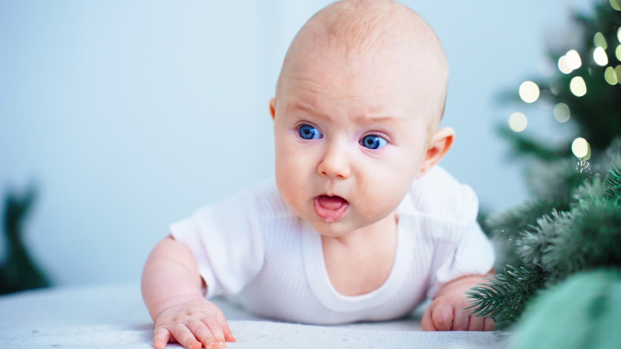 Søt baby med blå øyne under magetid ved juletreet