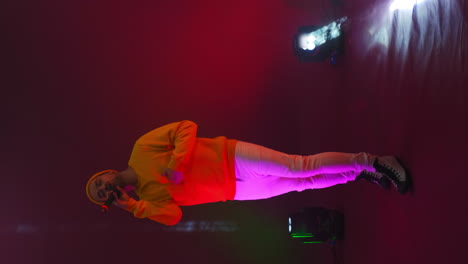 Vertical-video.-Funny-male-rap-artist-sings-and-dances-into-a-microphone-on-a-stand-in-the-neon-light-of-lamps-and-in-the-Studio-on-a-colorful-bright-background