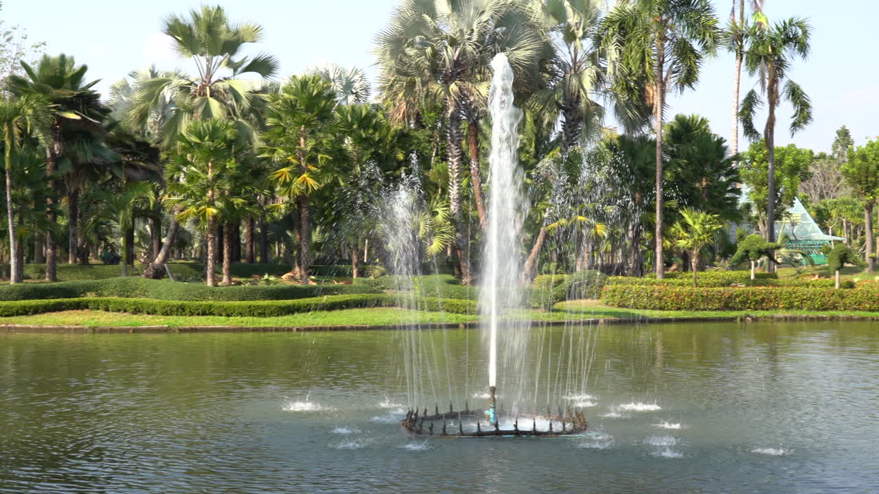 una vista panorámica de una fuente rociando agua en un estanque con un puente arqueado en el fondo rodeado de hermosas plantas