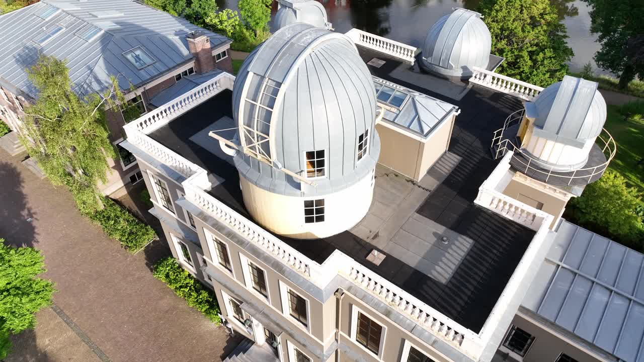 Aerial zoom in focusing on the historic Leiden Observatory domes and architectural details surrounded by trees in Leiden, Netherlands