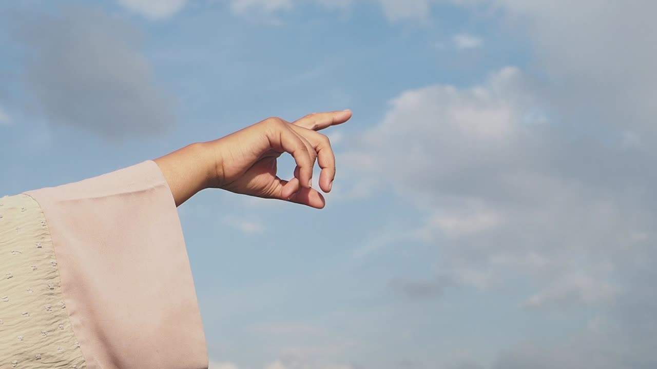 Hand pointing towards a cloudy blue sky