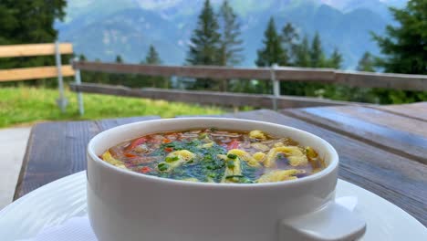 traditional austrian frittatensuppe with a beautiful summertime mountain view in tyrol austria, delicious hot comforting soup in serfaus fiss ladis, 4k shot