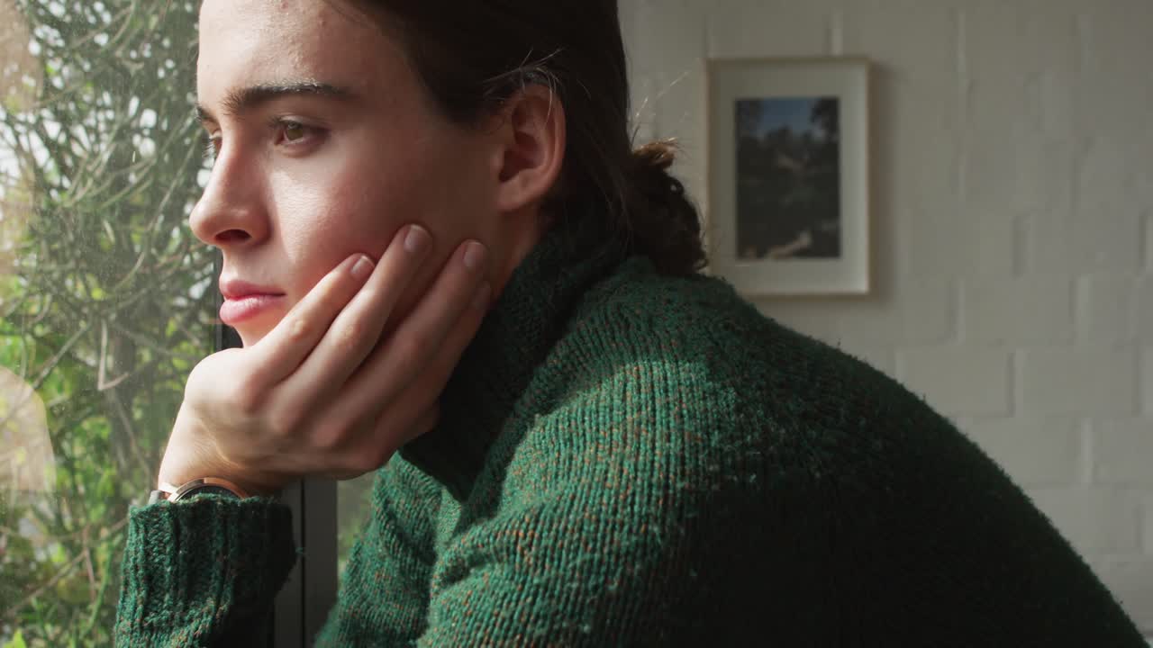 mujer transgénero caucásica no binaria mirando por la ventana y pensando