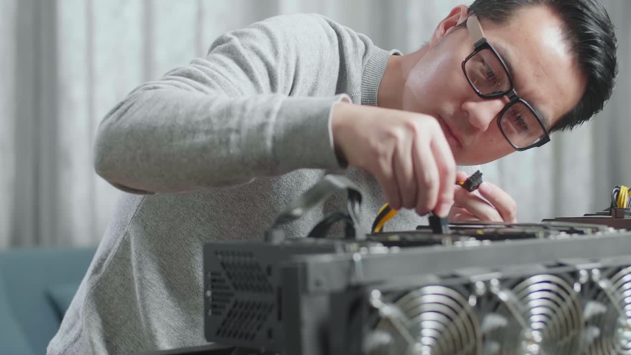 안경을 쓴 아시아 남자가 암호화폐를 채굴하기 위해 광산 기지의 전원 케이블을 연결합니다.