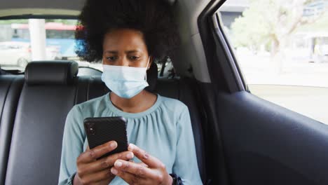 mujer de negocios afroamericana con máscara facial usando un teléfono inteligente