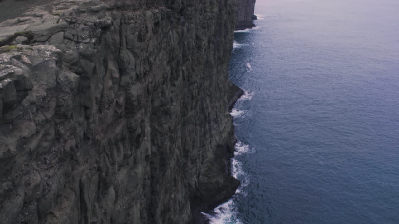 revelar la inclinación hacia arriba de un increíble y espectacular paisaje de caída de acantilado con olas del océano atlántico norte chocando contra las rocas en las islas feroe