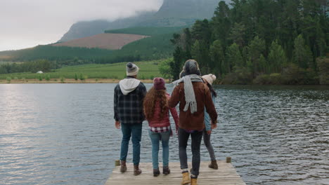 group of friends hugging on jetty by lake celebrating freindship reunion enjoying beautiful view wearing warm clothes on cloudy winter day 4k