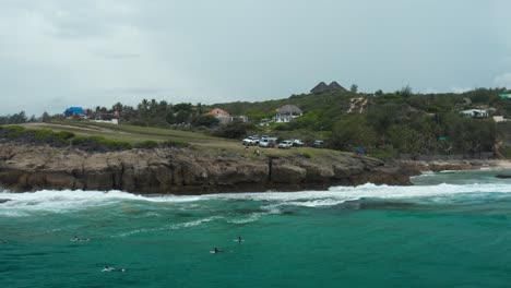 drone shot flying backwards from a cliff over the ocean above surfers - tofo, mozambique.
