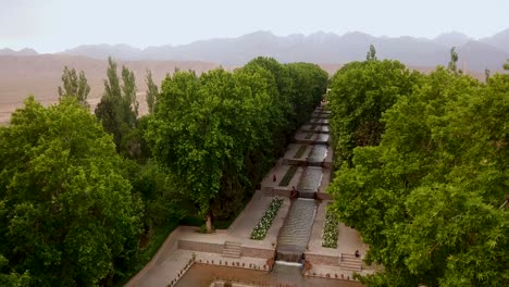 Aterrizaje-Aéreo-En-Un-Hermoso-Jardín-Con-Flujo-De-Agua-Corriente-En-Un-Desierto-Seco-Con-Paisaje-Montañoso