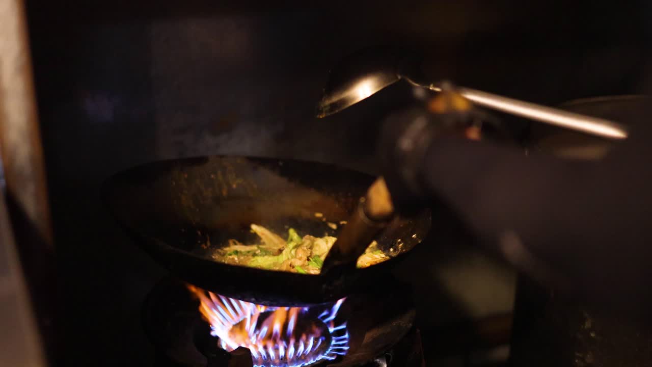 Uno chef cucina vigorosamente il sukiyaki thailandese in un wok fiammeggiante in una bancarella di street food notturna