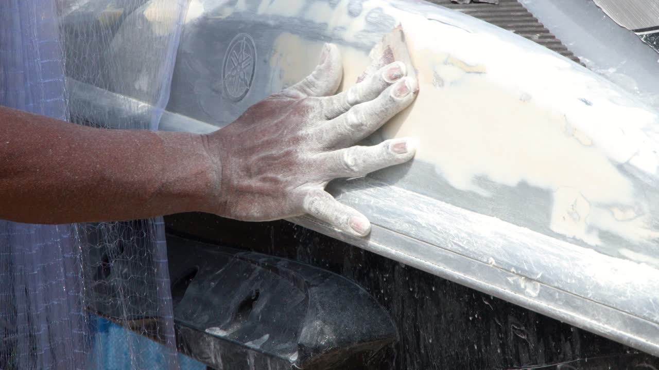 Close-up shot of a mechanic sanding body filler on a jet ski in Phuket, Thailand