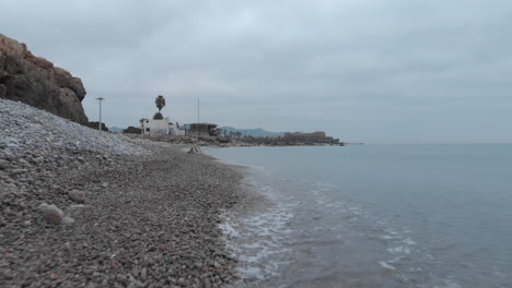 low drone shot glides forward along rocky shoreline of sea, capturing rugged beauty of coastline on an overcast day