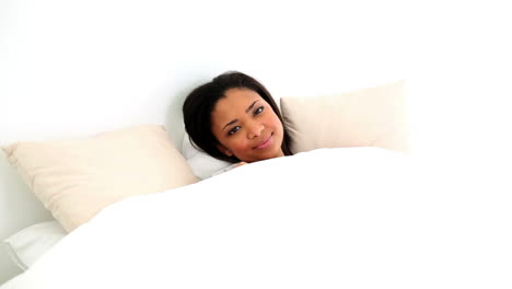 hermosa mujer de cabello oscuro acostada en su cama despertando