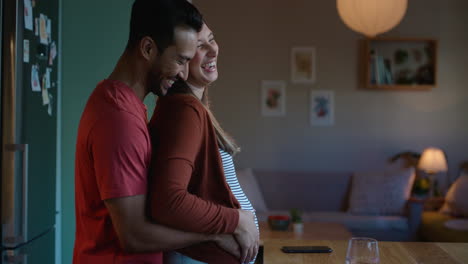 Pregnant,-hug-and-couple-in-a-kitchen-at-night