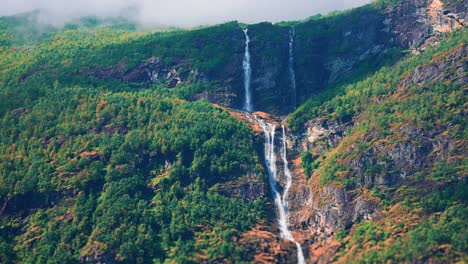 cascada de dos niveles en los acantilados cubiertos de bosque por encima del lago loenvatnet