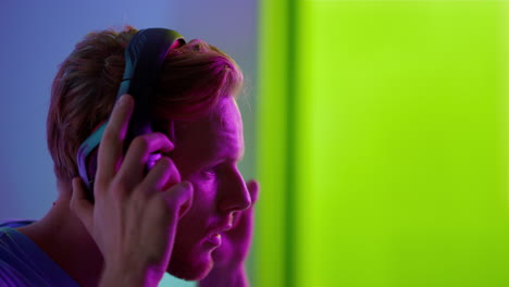 neon guy putting headphones at cyberspace room closeup. focused ginger guy