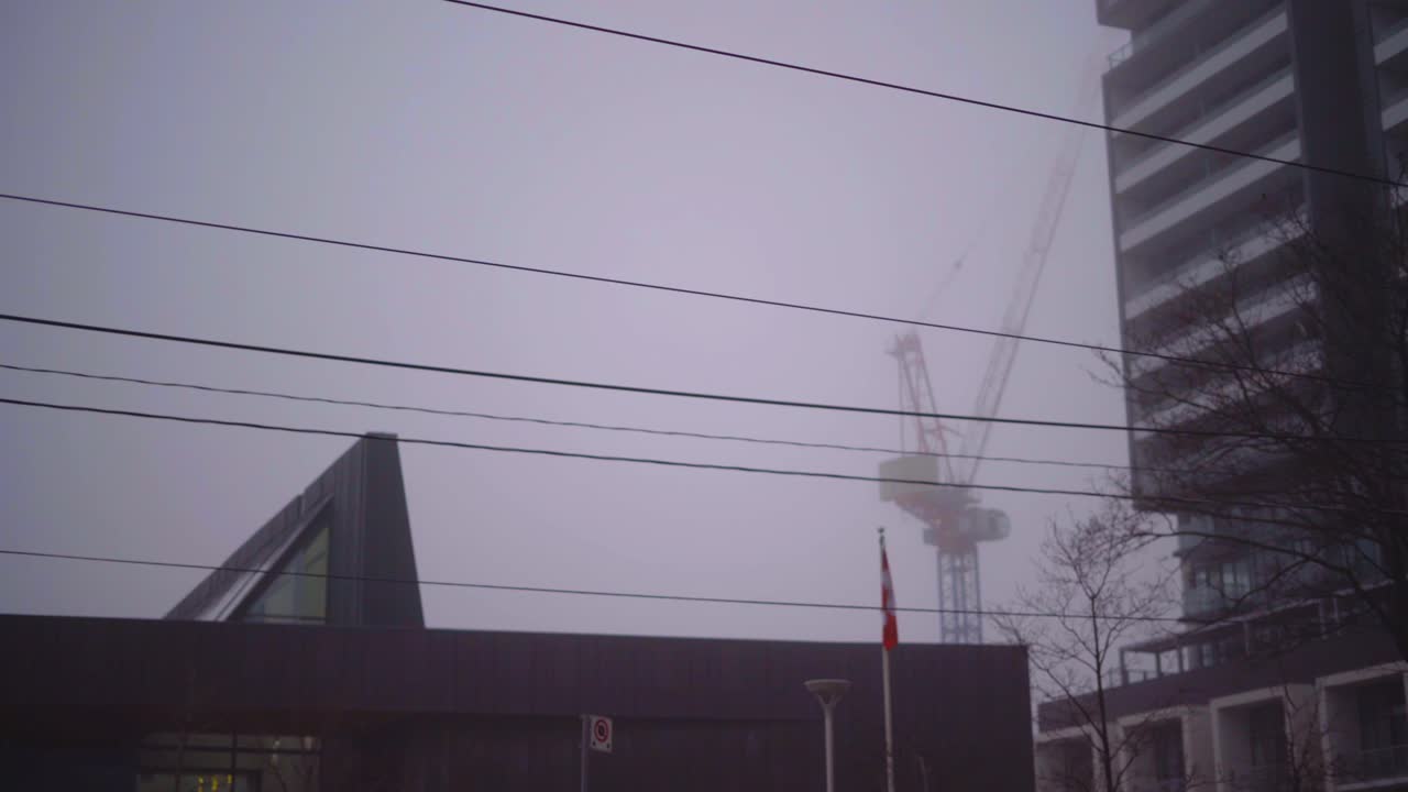 Crane for Construction in City Fog - Foggy City with crane in background through power lines and behind building for constructing new development condo during foggy morning - panning shot