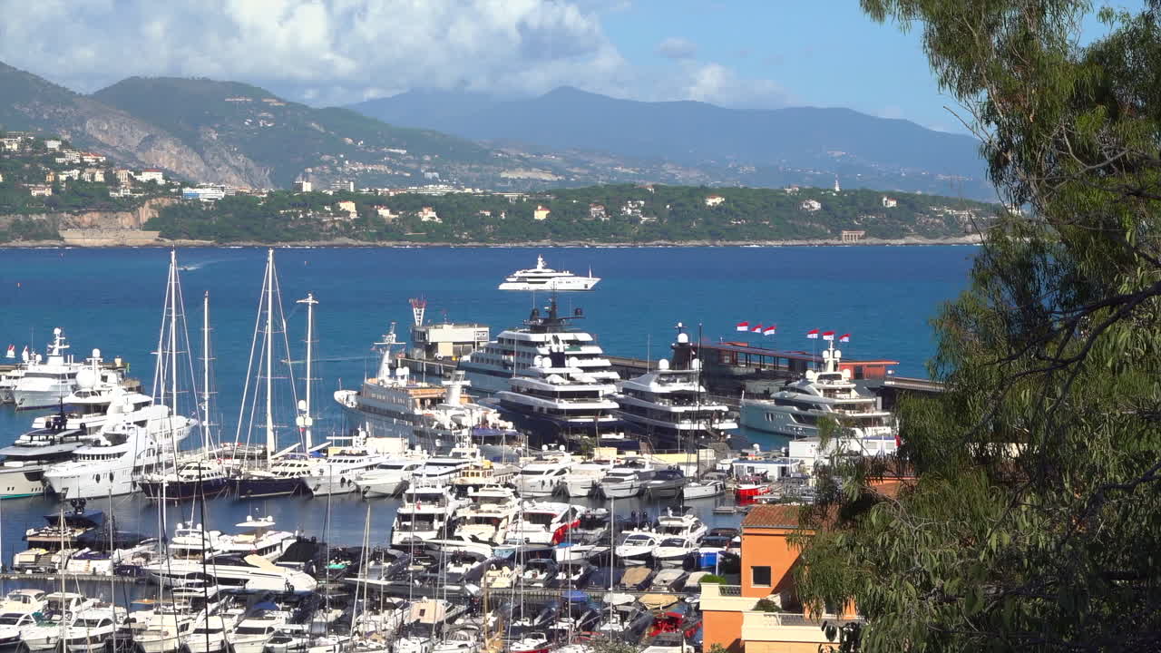 Yacht di lusso ormeggiati a Port Hercule, Monaco, con colline verdi e il mare blu sullo sfondo