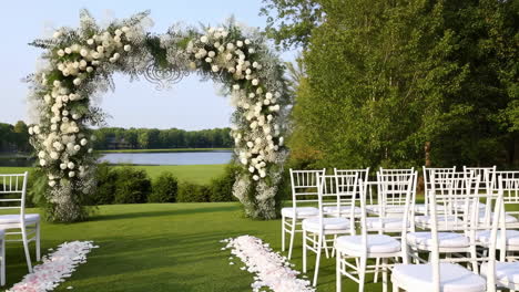 elegant outdoor wedding ceremony setup with floral arch by a lake