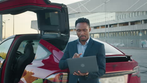 close up of african american man holding wireless laptop while leaning on his luxury red car young