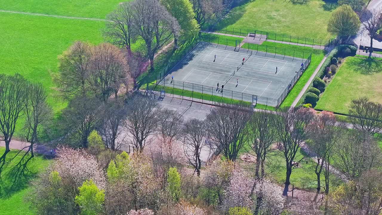 Drone symmetrical layout of trees and lawns boardering tennis courts in city park space, Clifton Park UK