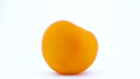 one whole big yellow tomato with water drops is rotating on the turntable isolated on the white background. close-up. macro.