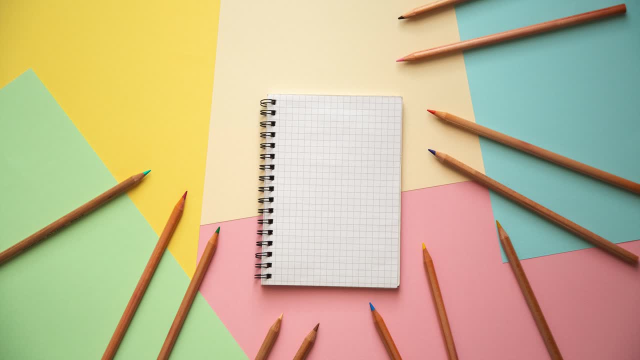 Stop motion of a notebook and wooden pencils on pastel colored paper