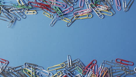 overhead view of scattered colourful paper clips with copy space on blue background, in slow motion