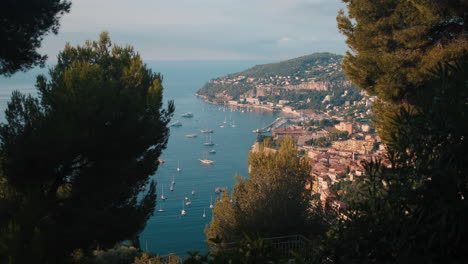 Beautiful-wide-shot-of-old-coastal-city-Beaulieu-sur-mer-behind-trees-and-plants-during-sunny-day