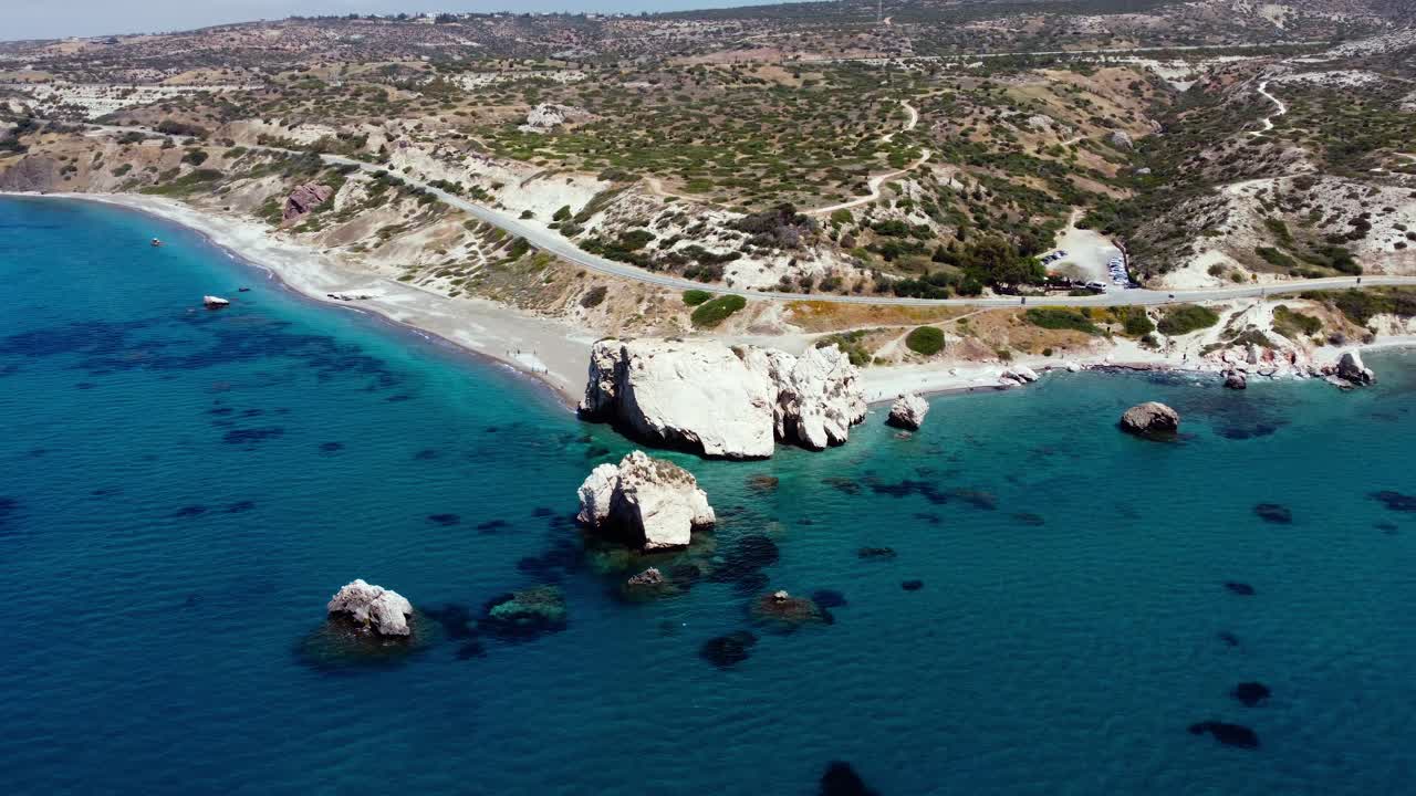 Sweeping aerial view over the iconic sea‑stack of Aphrodite’s Rock at Petra tou Romíou, Cyprus, where turquoise Mediterranean waters lap dramatic coastal cliffs in a legendary dawn setting