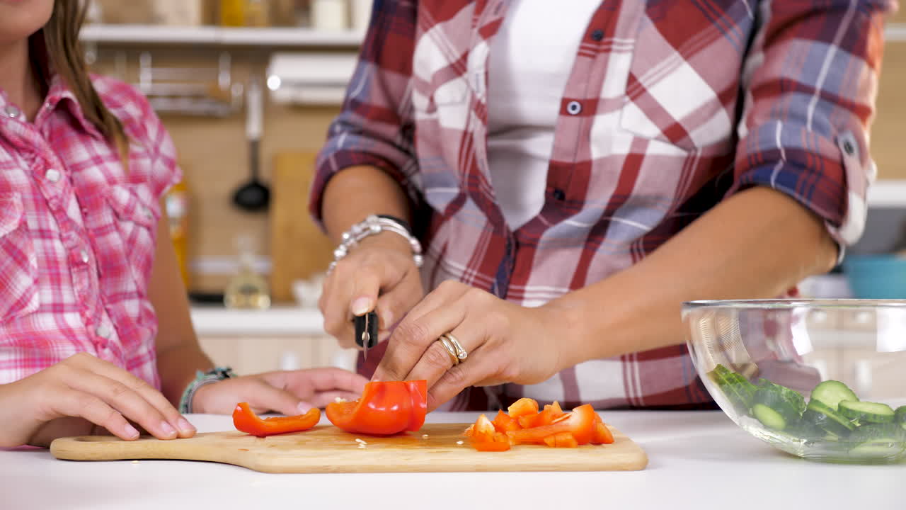 A mother and daughter cutting vegetables for a salad